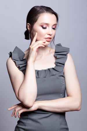 Portrait of young woman in gray dress on gray background. Bunette female with hands near face and earring in the ear. beauty makeup concept.の写真素材