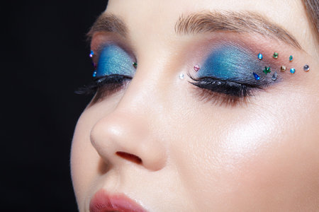 Closeup shot of human woman face with eyes closed. Female with natural face and eyes beauty makeup with blue eye shadow make up and rhinestones.の写真素材