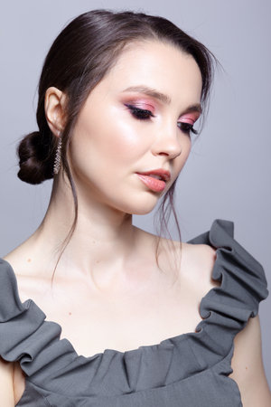 Portrait of young woman in gray dress on gray background. Bunette female side view with hair knot and earring in the ear. beauty makeup concept.の写真素材