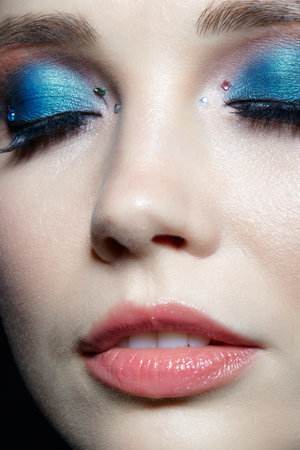 Closeup shot of human woman face with eyes closed. Female with natural face and eyes beauty makeup with blue eye shadow make up and rhinestones.の写真素材