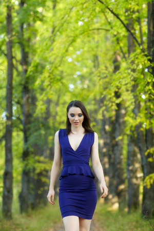 Female in blue dress walking along autumn linden tree alley. Path under yellow trees with falling autumn leaves. Sunny autumn day. The rays of the sun shine through the trunks and crowns of trees.の写真素材