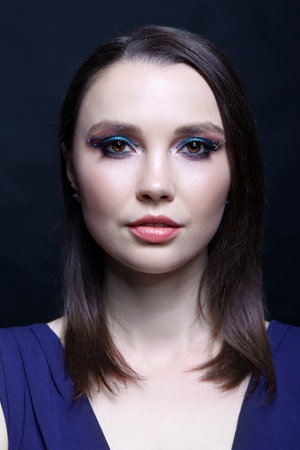 Portrait of beautiful brunette female with blue eye shadow make up and rhinestones. Young woman in blue dress on black background.の写真素材
