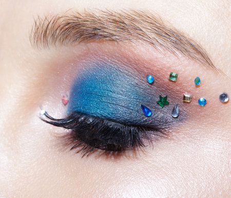 Closeup macro shot of closed human female eye with blue eye shadow make up and rhinestones. Woman with natural evening vogue face beauty makeup.の写真素材
