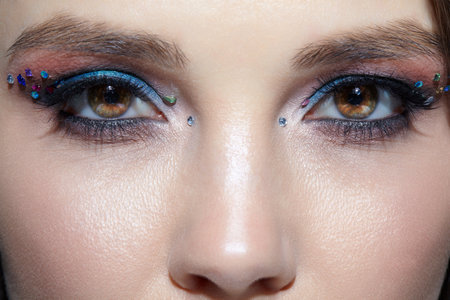 Close up shot of human woman face. Female with natural face and eyes beauty makeup with blue eye shadow make up and rhinestones.の写真素材