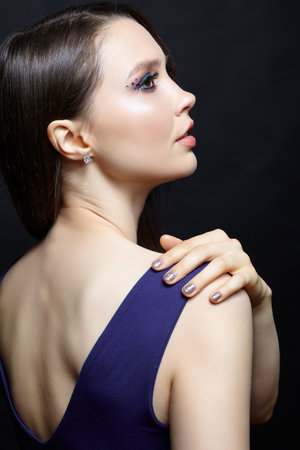 Portrait of beautiful brunette woman with blue eye shadow make up and rhinestones. Female with hand on shoulder. Nails with sparkling glitter fingernails manicureの写真素材