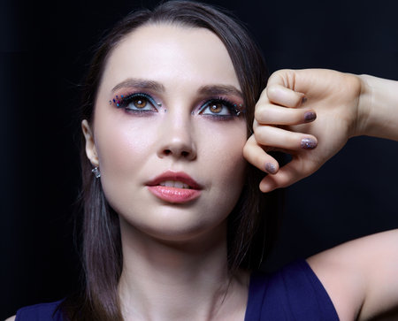 Close-up portrait of beautiful brunette with blue eye shadow make up and rhinestones. Hand near face. Nails with sparkling glitter fingernails manicureの写真素材