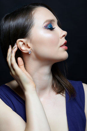 Portrait of a young woman on gray background. Female posing with hand near face. Makeup with blue eye shadows. In the ear is an earring with a white crystal stone.の写真素材