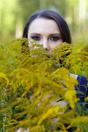Romantic portrait of female in blue dress in nature. Brunette woman in the field of yellow flowers Solidago canadensis (Canada goldenrod or Canadian goldenrod) flowers.の写真素材