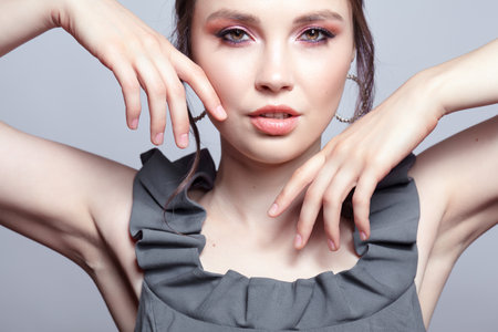 Portrait of young woman in gray dress on gray background. Bunette female with hands near face and earring in the ear. beauty makeup concept.の写真素材