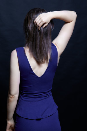 Young brunette woman in blue dress. Female view from the back side. Hand on head.の写真素材