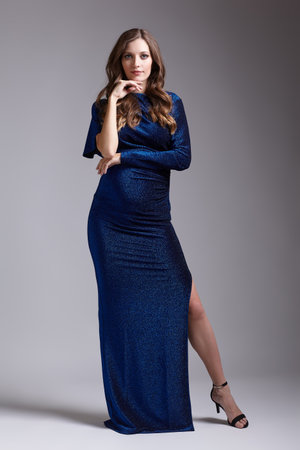 Portrait of young pretty pregnant woman on gray studio background. Female in blue sequin dress. One hand on hip, second near face.の写真素材