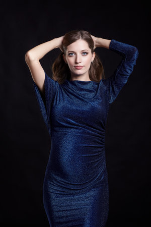 Portrait of young pretty pregnant woman on black studio background. Female in blue sequin dress with hands behind head.の写真素材