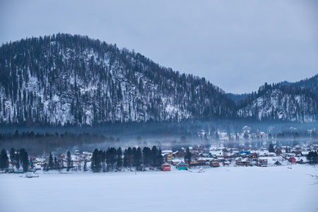 Houses on the bank of frozen Teletskoe lake under the chimney smoke. Iogach, Altai, Siberia, Russiaの写真素材