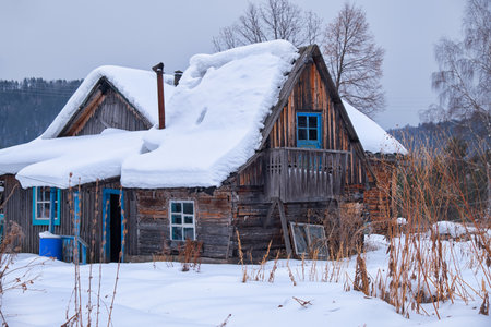 Old abandoned wooden house. The roof is covered with a thick layer of snow. Altai village Ust'-Lebed' in winter season. Siberia, Russia.の写真素材