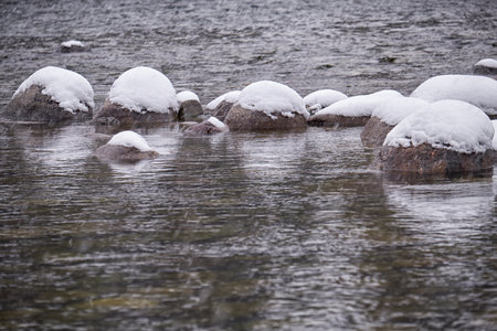 Stones with snow caps in the water of Altai Biya river under heavy snow in winter season.の写真素材