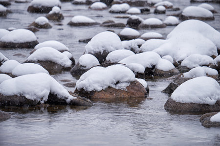 Stones with snow caps in the water of Altai Biya river under heavy snow in winter season.の写真素材