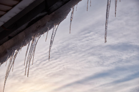 Dropping icicles on a warm spring day hang from the wooden roof of an old house and sparkle in the light on the Sun.の写真素材