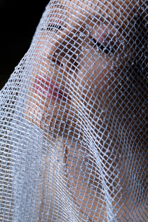 Portrait of a young woman covered with white mesh fabric. A woman hides her face behind a veil cloth. Female beauty concept.の写真素材