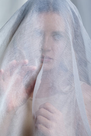 Portrait of a young woman covered with white mesh fabric. A woman hides her face behind a veil...