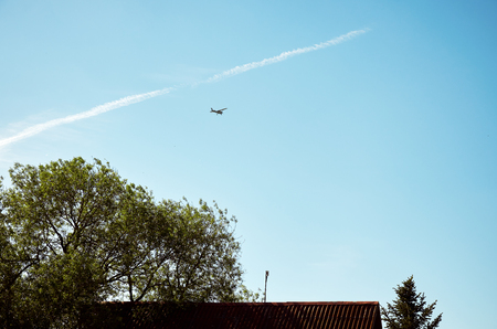 A plane flying in the sky above the roof of the house.の写真素材