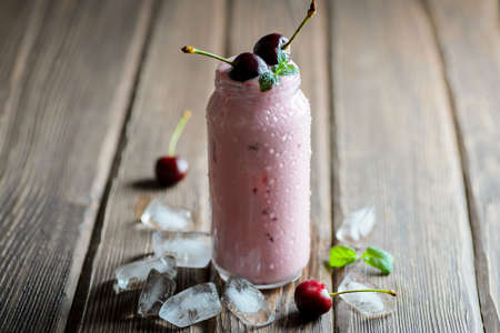 Yoghurt dessert with cherry and ice cubes on wooden tableの写真素材