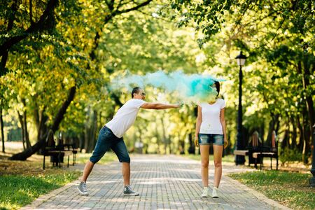 Young and beautiful, hipster couple funny playing in the park on holi color festival with colour paint powder and throw each other with colour paint powder. Dressed in white T-shirts and denim shorts.の写真素材