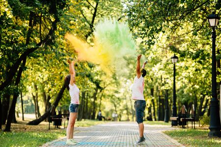 Young and beautiful, hipster couple funny playing in the park on holi color festival with colour paint powder. Dressed in white T-shirts and denim shorts.の写真素材