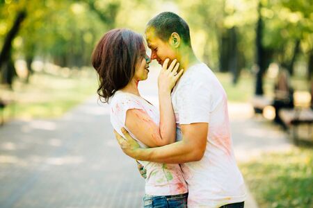 Beautiful, hipster couple funny playing in the park on holi color festival with colour paint powder. They are lovely looking into each other's eyes. Dressed in white T-shirts and denim shorts.の写真素材
