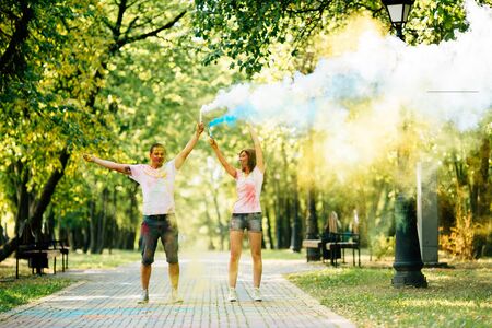 Young and beautiful, hipster couple funny playing in the park on holi color festival with colour paint powder and color smoke. Dressed in white T-shirts and denim shorts.の写真素材