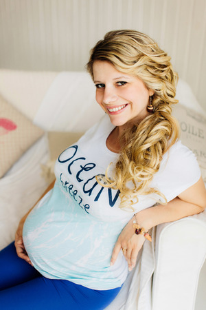 Young beautiful pregnant woman sitting on white sofa and lovely smiling. Blue and  white colors.の写真素材