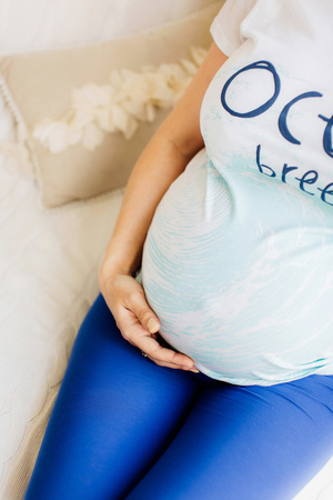 Young beautiful pregnant woman hold hands on belly sitting on white sofa. Blue and  white colors.の写真素材