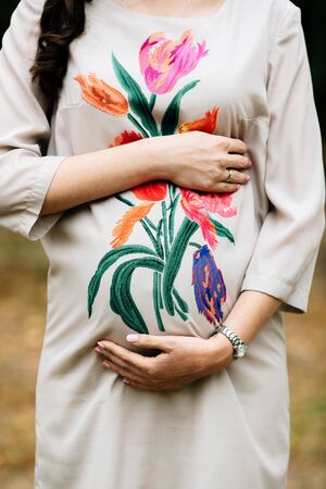 Expectant young mother holds pregnant belly in nature in the park.