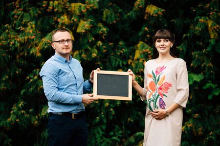 Expecting pregnant happy stylish couple holding a blank charcoal board.の写真素材
