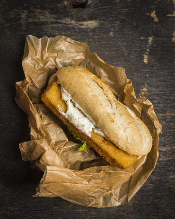 bun with fish and sauce in a paper on a wooden table top viewの写真素材