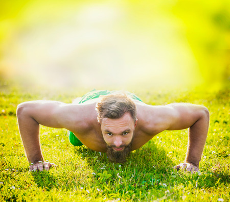 Sports man with brown hair and a beard on a natural background, performing push-upsの写真素材
