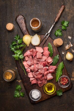 raw uncooked meat sliced on vintage cutting board with fresh ingredients for cooking stew or goulash on rustic wooden background, top viewの写真素材