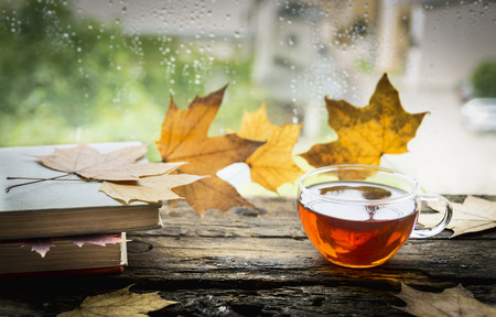 cup of tea on a wooden window sill with books and autumn leaves on a natural backgroundの写真素材