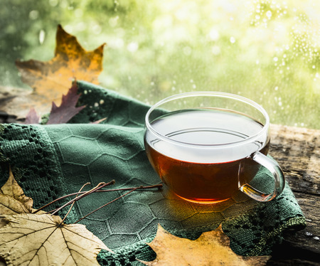 cup of tea on a wooden window sill with a green cloth and autumn leaves on a natural backgroundの写真素材
