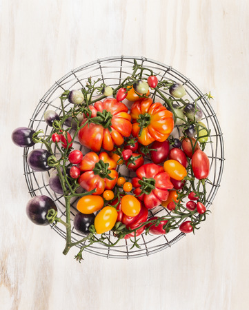different tomatoes in a basket on white wooden backgroundの写真素材