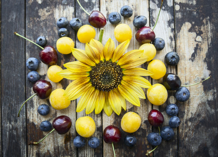 fresh different berries on a wooden background with sunflower, top viewの写真素材