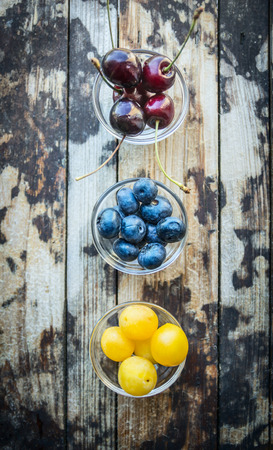cherries, apricots, currants in a bowls, on a wooden background, top viewの写真素材
