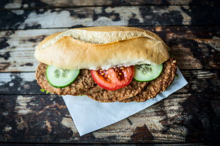 bun with meat cutlets with cucumber and tomatoes on a wooden background, top view, toningの写真素材