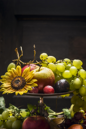 Different summer fruits in an iron bowl with a sunflower on a wooden background, close upの写真素材