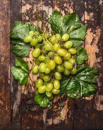 Fresh bright grapes on a branch with leaves on dark wooden background, top viewの写真素材