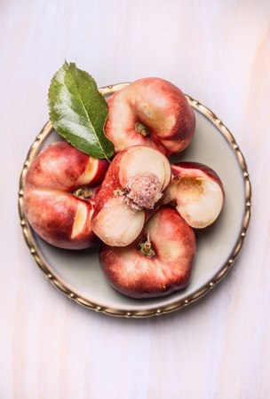 sliced fresh peach with leaf in plate on a white wooden background, top viewの写真素材
