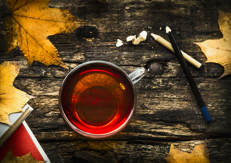 cup of tea with autumn leaves, books and pencils on wooden background, top viewの写真素材
