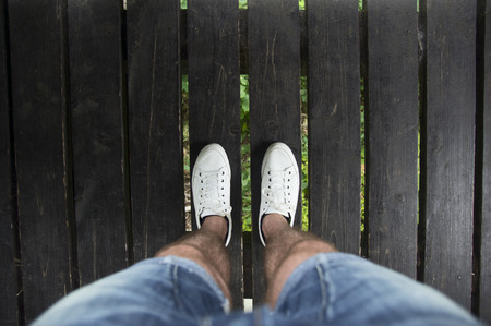 male legs in shorts and white shoes on a wooden bridge,top view