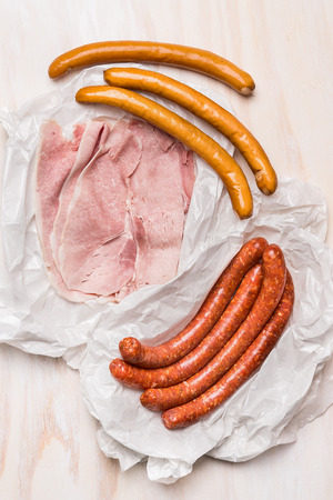 different long sausages and ham in a crumpled paper packaging on rustic wooden background, top viewの写真素材