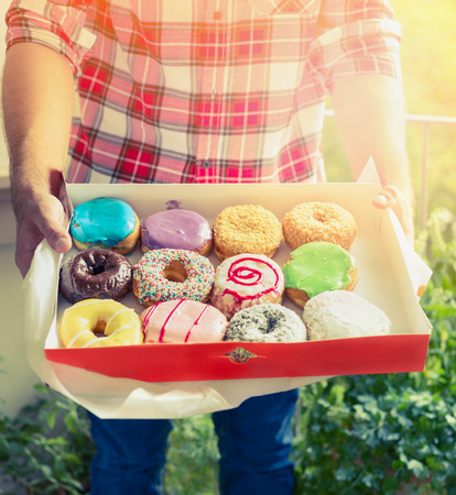 young man in plaid shirt holding colorful glazed donuts on background of a sunny nature background, retro tonedの写真素材