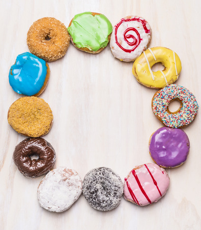 round frame of colorful doughnuts on white wooden background, top viewの写真素材